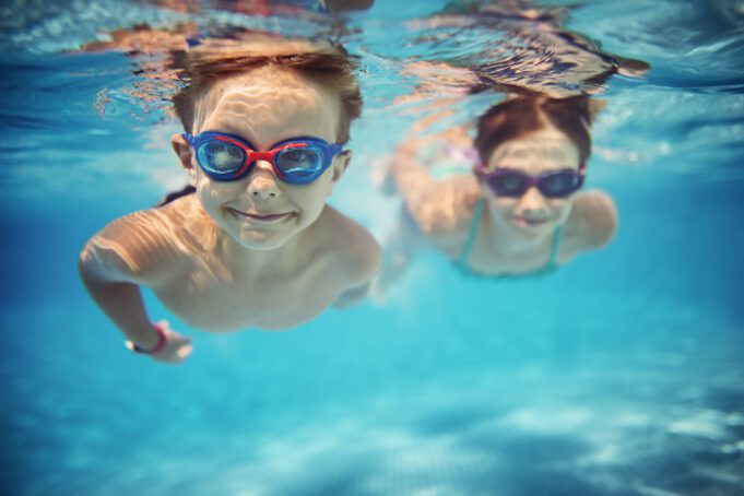 Två barn simmar under vattnet i simbassäng
